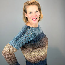 Load image into Gallery viewer, A smiling woman with blonde hair wearing a crocheted long-sleeve sweater with a color gradient from blue to brown, posed against a solid gray background.
