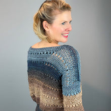 Load image into Gallery viewer, A woman shown from the back wearing a crocheted sweater with a blue-to-beige gradient, photographed against a plain gray studio background.

